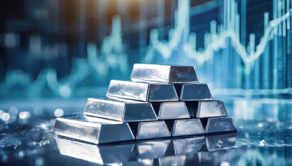 Stacked silver ingots on a reflective surface with a blurred stock chart backdrop, suggesting wealth or precious metal investment