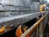 Aura Minerals-Aktie: Starke Dividenden, wachsendes Geschäft Underground mine tunnel with a conveyor belt carrying rocks, rocky walls, and safety railing along the path.