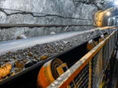 Aura Minerals-Aktie: Starke Dividenden, wachsendes Geschäft Underground mine tunnel with a conveyor belt carrying rocks, rocky walls, and safety railing along the path.
