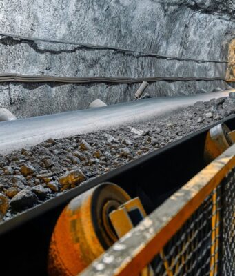 Aura Minerals-Aktie: Starke Dividenden, wachsendes Geschäft Underground mine tunnel with a conveyor belt carrying rocks, rocky walls, and safety railing along the path.