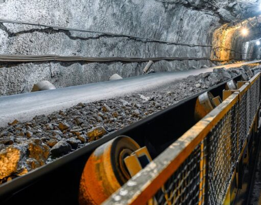 Aura Minerals-Aktie: Starke Dividenden, wachsendes Geschäft Underground mine tunnel with a conveyor belt carrying rocks, rocky walls, and safety railing along the path.