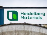 Heidelberg Materials-Aktie -14% im Juniverlauf Large Heidelberg Materials sign with green logo on a white panel against a blue industrial building exterior.