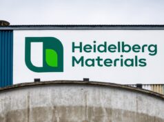 Heidelberg Materials-Aktie -14% im Juniverlauf Large Heidelberg Materials sign with green logo on a white panel against a blue industrial building exterior.