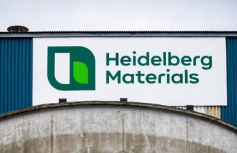 Heidelberg Materials-Aktie -14% im Juniverlauf Large Heidelberg Materials sign with green logo on a white panel against a blue industrial building exterior.
