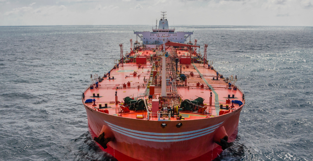 öl-tanker1 Front view of a large red oil tanker sailing in calm blue sea, deck filled with equipment and cranes.