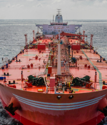 Neue Iran-Eskalation: Beginnt jetzt die zweite Ölpreis-Welle? Front view of a large red oil tanker sailing in calm blue sea, deck filled with equipment and cranes.