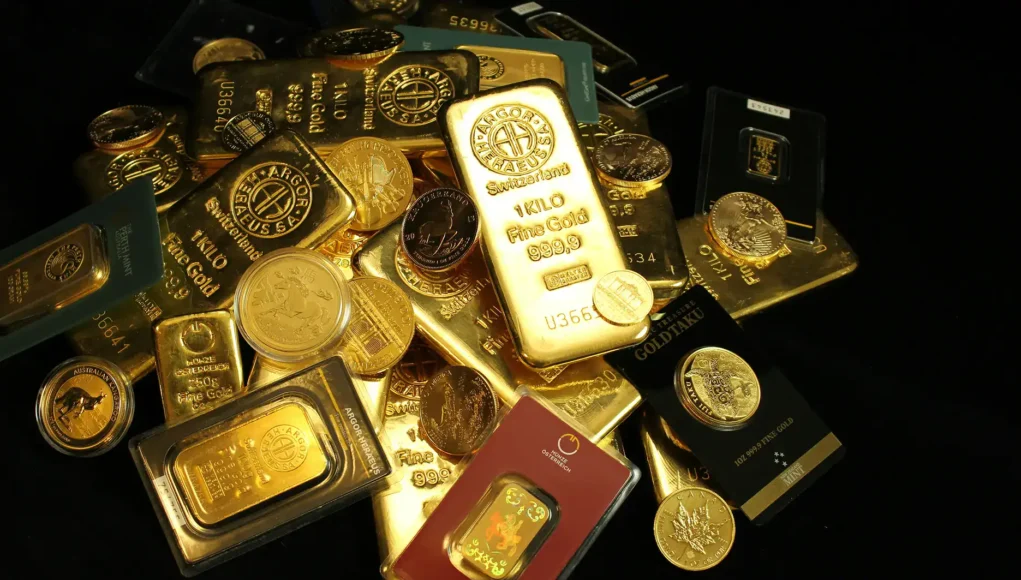 Pile of gold bars and coins on a dark background, with a prominent 1 kilo gold bar stamped 999.9 fine gold.