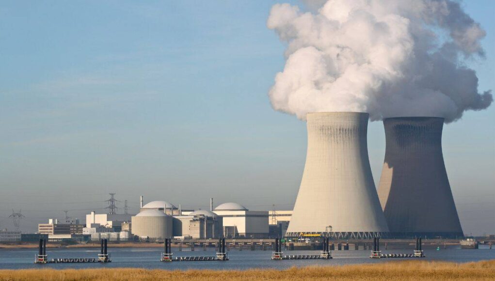 Cameco-Aktie-Diese-Kursziele-lassen-Anleger-aufhorchen.jpeg Nuclear power plant with two large cooling towers releasing steam, set near a waterway with industrial buildings in the background.
