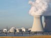 Cameco-Aktie: Zahlen enttäuschen – ist der Boden nah? Two large hyperbolic cooling towers at an industrial power plant emit steam into the sky, with additional buildings and water in the foreground.