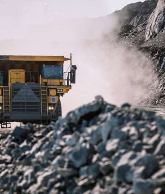 Rio Tinto-Aktie & der Kupferpreis in luftigen Höhen Yellow mining dump truck drives through a dusty rocky quarry with steep rock faces on either side