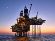 Chevron-Aktie: Öl-Boom trifft auf KI-Fantasie Offshore oil platform lit up at dusk, standing on stilts above calm ocean with a crescent moon in the sky.