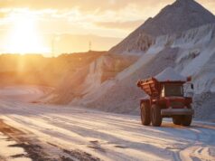 Intrepid Potash: Kleine Kali-Aktie mit großem Gewinnhebel Red off-road mining dump truck drives along a sandy quarry with large rock piles at sunset.