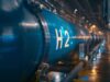 Nel ASA Aktie: Wie weit geht der Absturz noch? Blue industrial pipeline labeled H2 runs through a modern plant, indicating hydrogen piping.