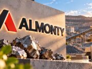 Almonty-Aktie: Kippt der Abwärtstrend oder bleibt es dabei? Almonty corporate sign with illuminated logo at a mining site, stacked rocks in foreground and industrial conveyor in background.