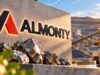 Almonty-Aktie vor dem Comeback – schlagen Käufer jetzt zu? Almonty company sign on a stone wall beside a mining site with rocks and a tungsten block marked W 183.84 in the foreground at sunset.
