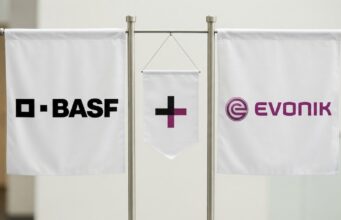 Evonik-Aktie: Kommt jetzt doch eine schnelle Übernahme? Three white banners on a metal stand showing BASE on the left, a central banner with a black plus and purple vertical bar, and the EVONIK logo on the right.