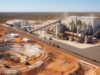Lynas Rare Earths-Aktie -7%: Warum die miese Laune? Open-pit mining and processing plant in a desert landscape with conveyors, silos, and heavy machinery nearby rail tracks.
