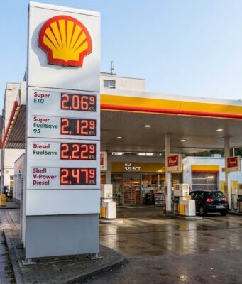 Shell-Aktie: Noch kaufen oder jetzt rausgehen? Shell gas station on a city street with a tall price board showing €2.06/L, €2.12/L, €2.22/L, and €2.47/L as of today, and wet pavement reflecting lights.