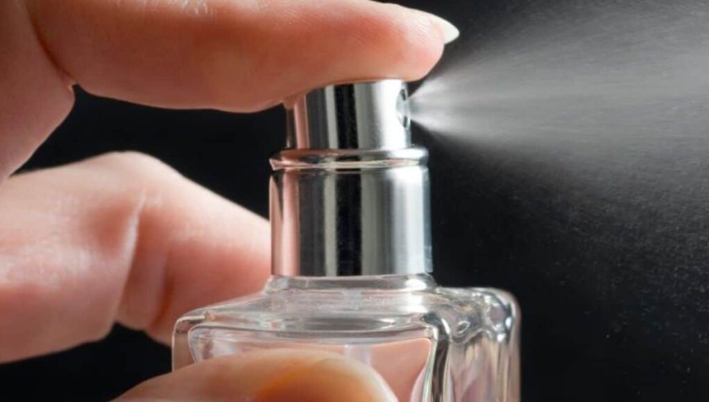 Symrise-Aktie-40-seit-Jahresanfang-Was-koennte-jetzt-ratsam-sein.jpeg Close-up of a hand pressing a perfume spray nozzle and releasing mist from a glass bottle