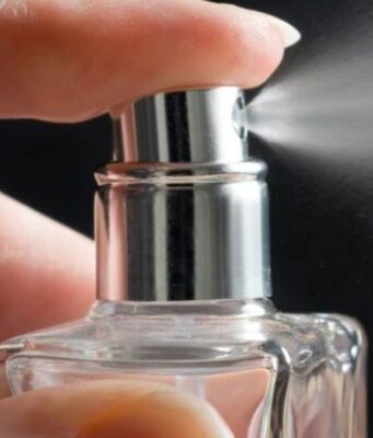 Symrise-Aktie +40% seit Jahresanfang: Was könnte jetzt ratsam sein? Close-up of a hand pressing a perfume spray nozzle and releasing mist from a glass bottle