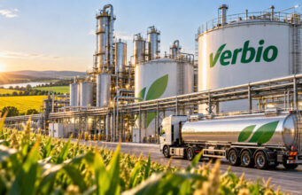 Verbio-Aktie +9%: Sind jetzt noch +50% mehr drin? Biorefinery complex with tall silver towers and large tanks marked Verbio, beside a farm field at sunset with a loading truck nearby